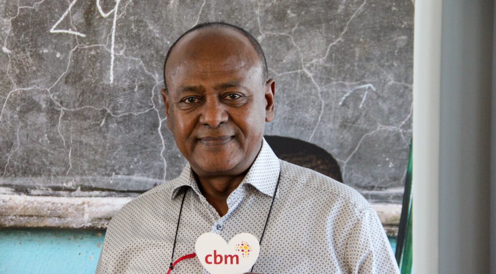 Dr Ketema, smiling, holds a heart with CBM written on it